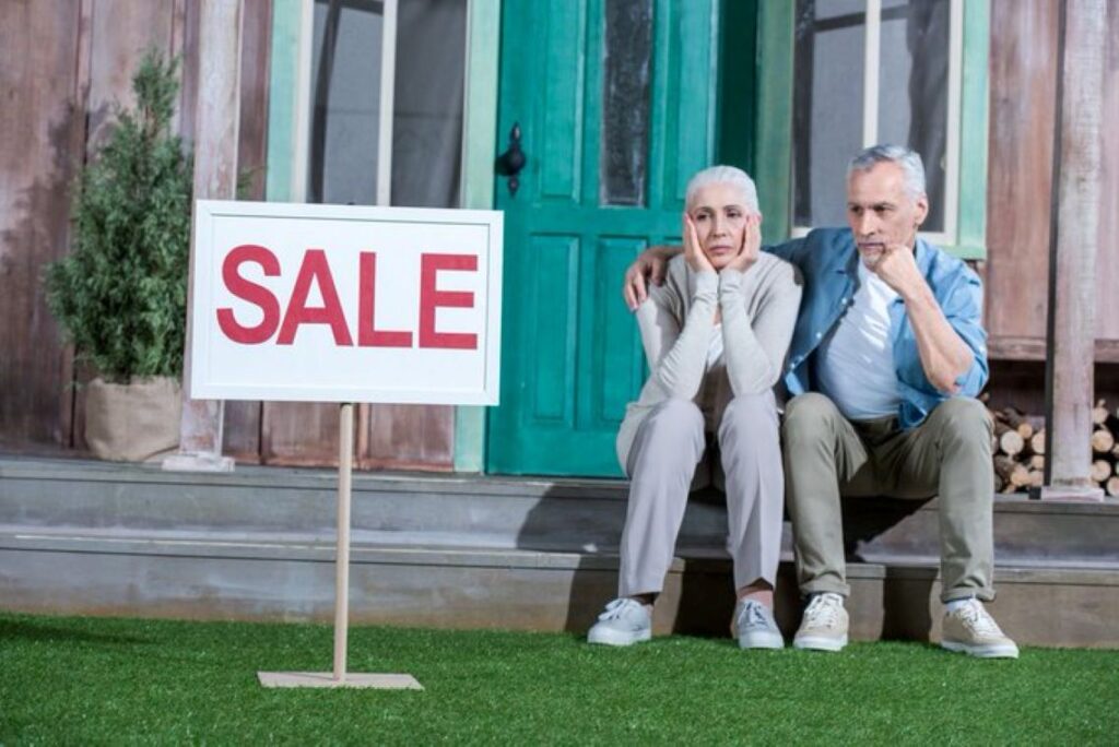 A man and woman staring at a “sale” sign outside their home