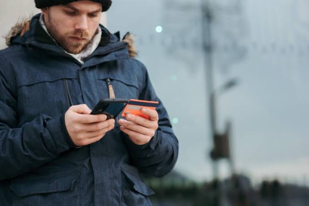 Pensive man holding credit card and browsing smartphone