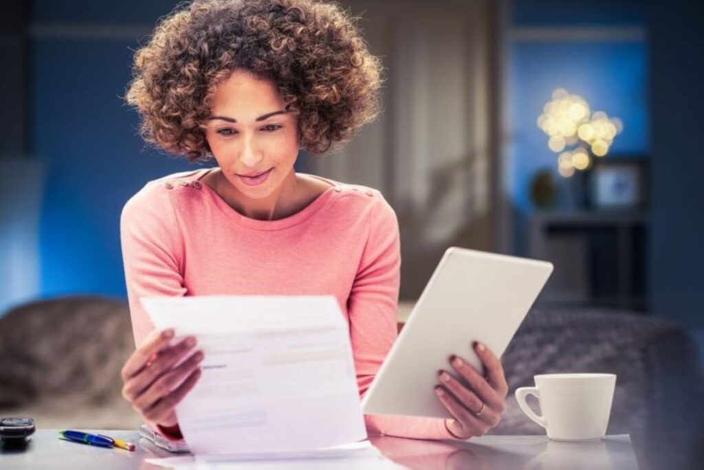 A woman holding a tablet and reading through a sheet of document