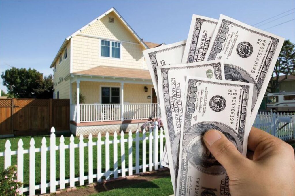 Hands holding $100 bills in front of a house