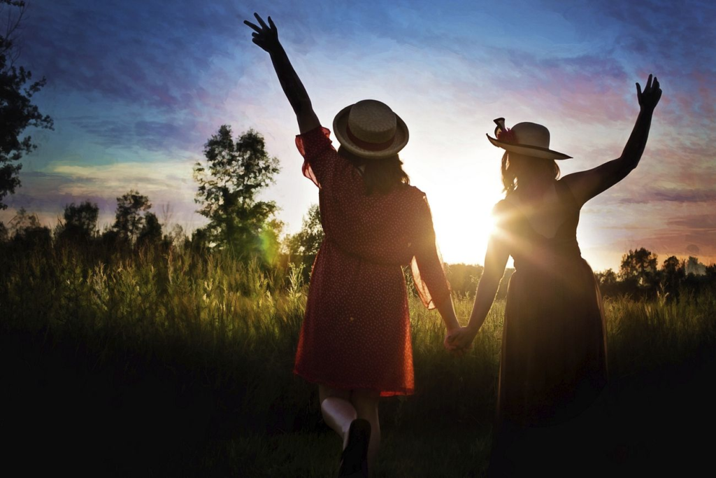 Two women holding hands and walking through a meadow at sunset