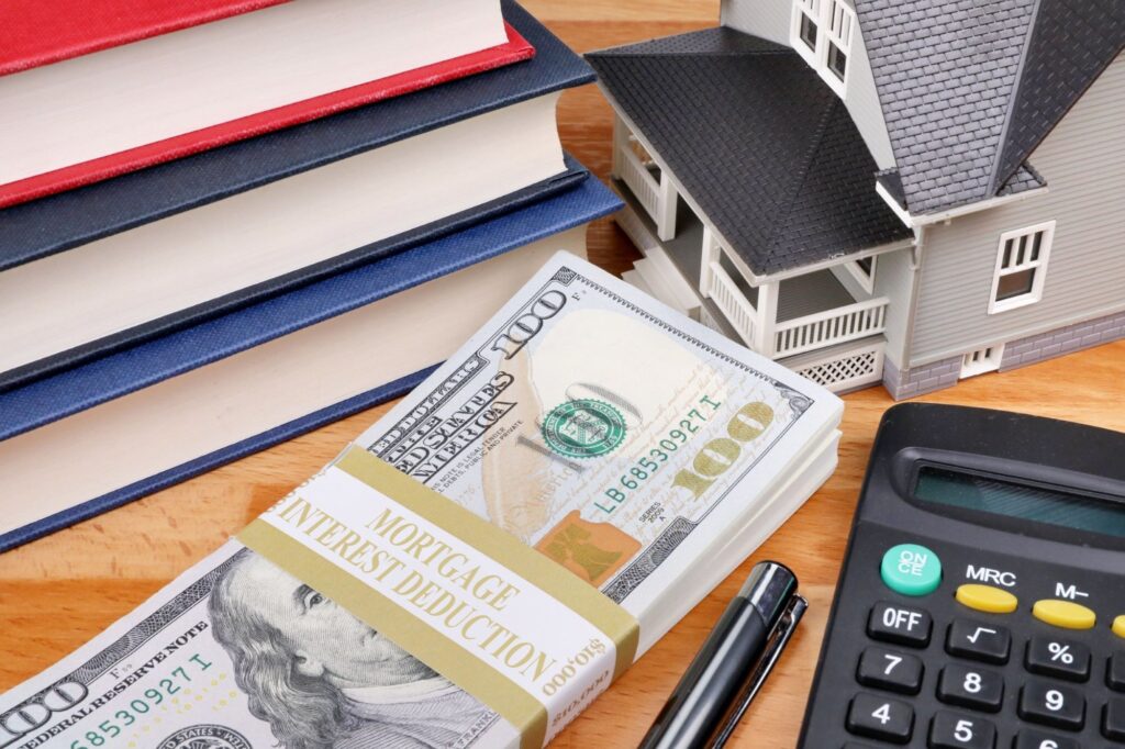 Wad of cash next to a calculator, books, and a model house