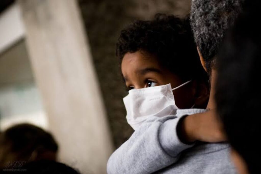 A child wearing a nose mask carried by an adult