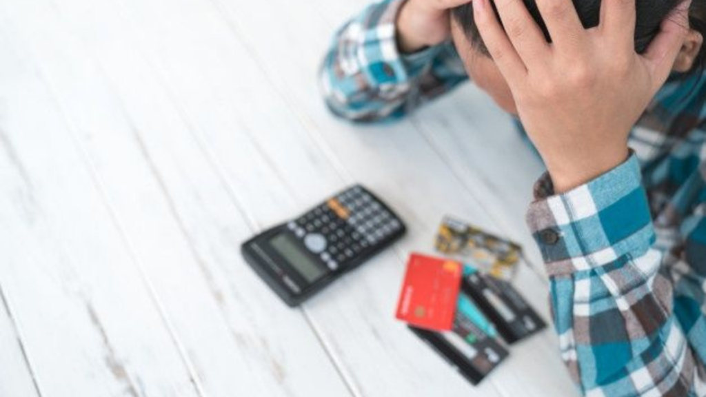 A man holding his hands over his head with credit cards and a calculator on the table