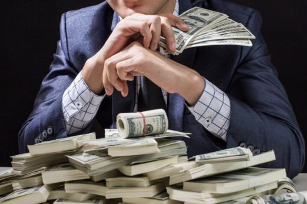 A man holding some cash and other bundles of cash on the table