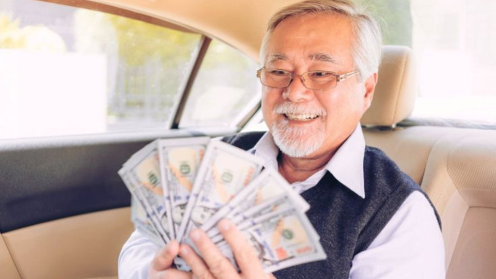 An elderly man holding some cash in the car