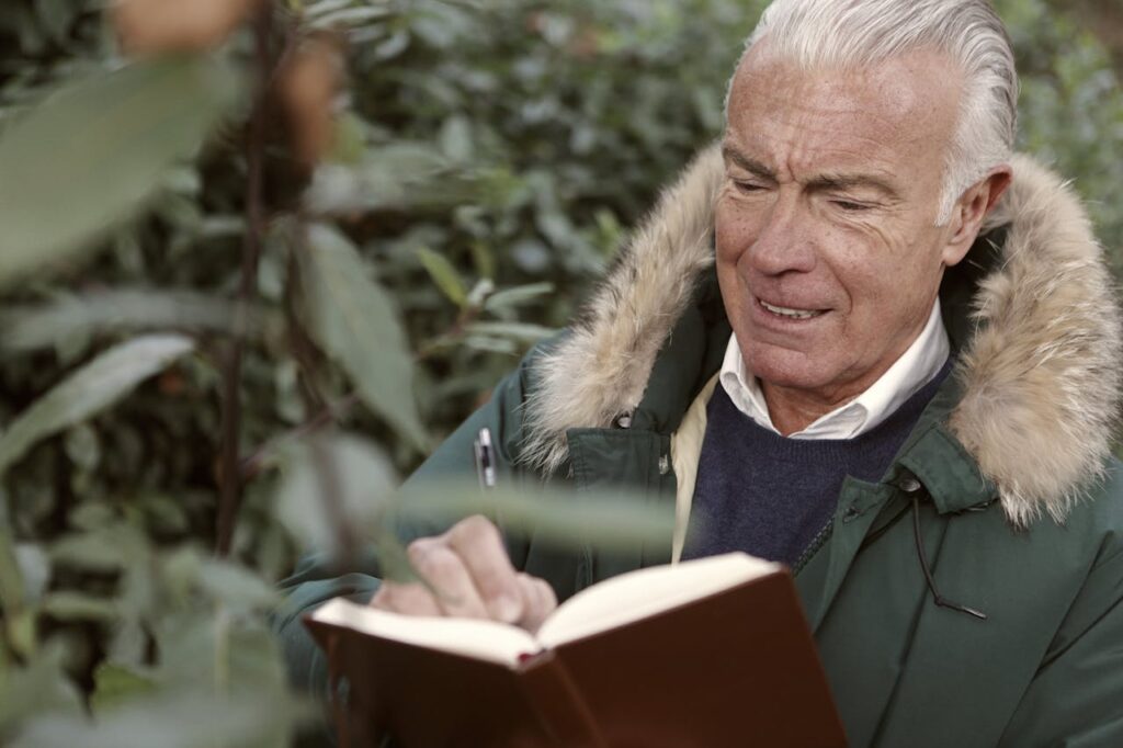 Man in Green Coat Writing On The Book