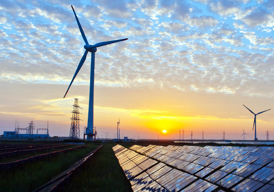 Solar cell panels in the foreground, wind turbines in the middle ground, and electricity pylons in the background