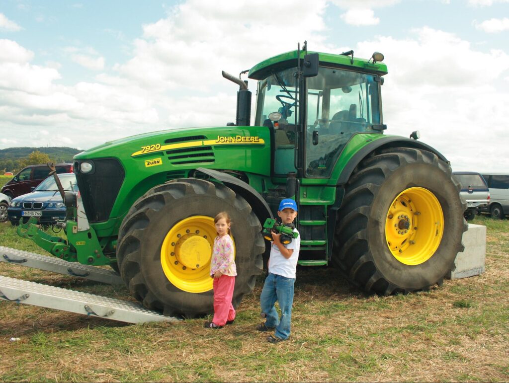 Two kids standing beside a Deere tractor