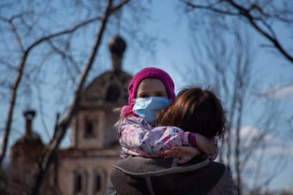 Child with nose mask on, on a woman's shoulder
