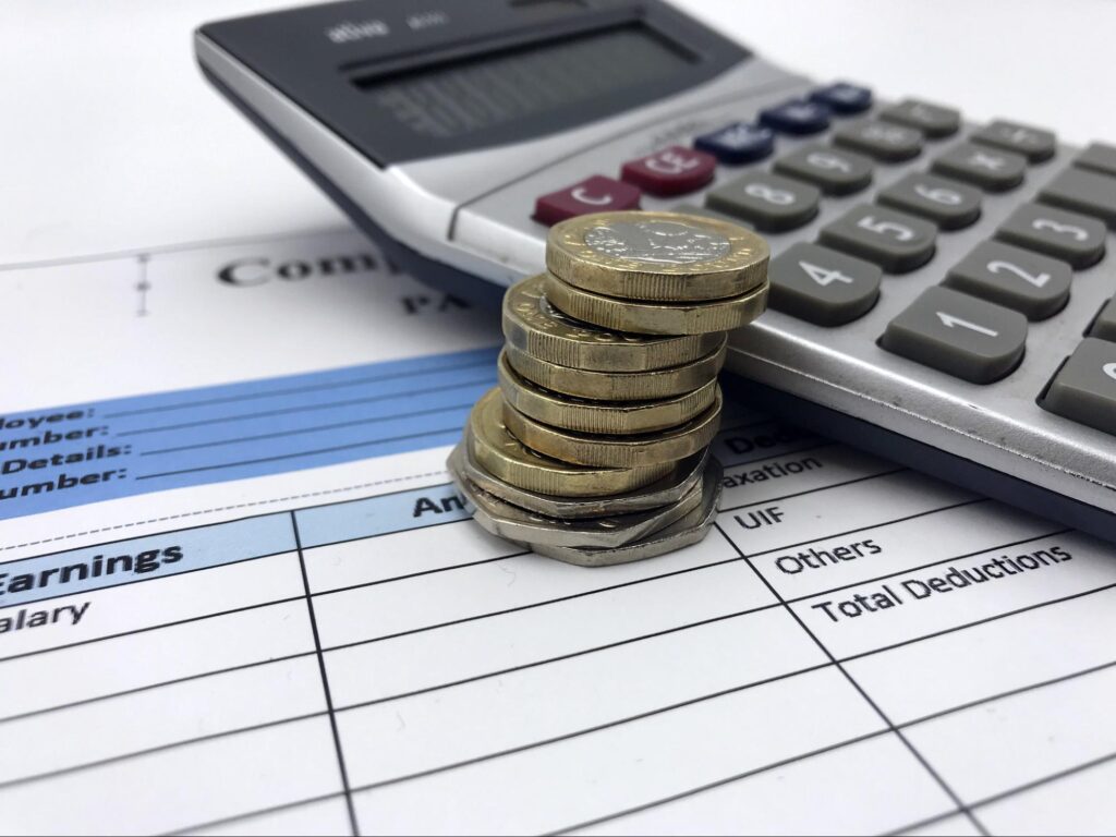 Stacked up coins and notes against a calculator and a wage slip