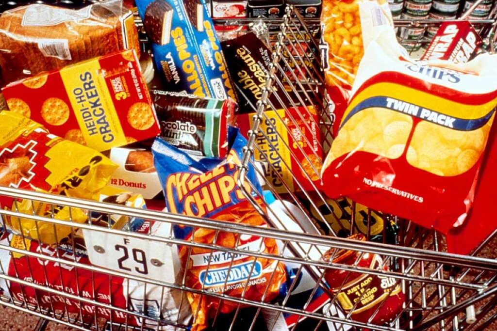 A shopping cart filled with "bad" snacks such as corn and potato chips, cookies, crackers, etc.