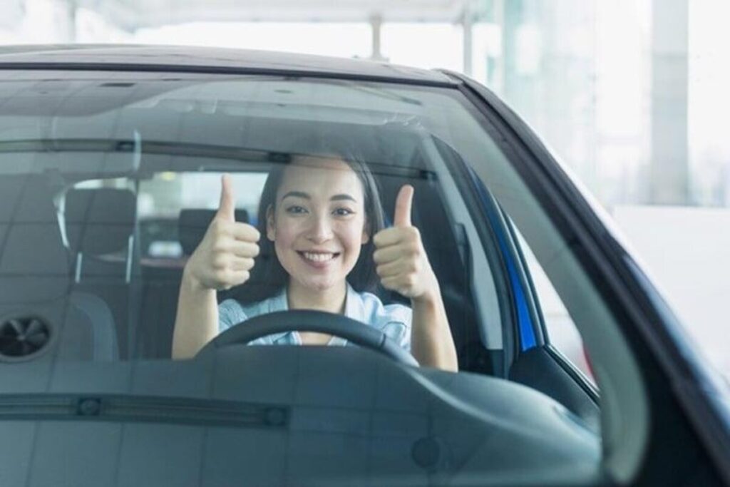 A young lady with double thumbs up in a car