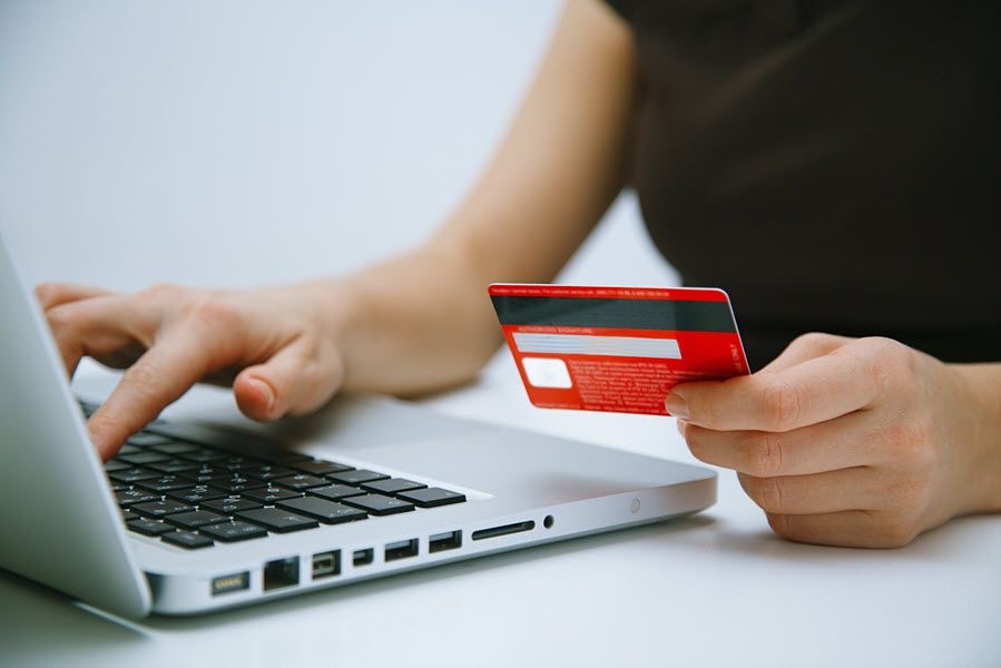 An image of a person holding a card and typing on a laptop