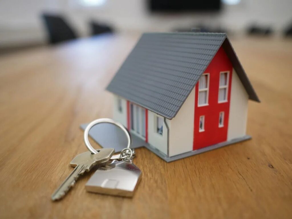 An image of in miniature house on a table with keys beside it