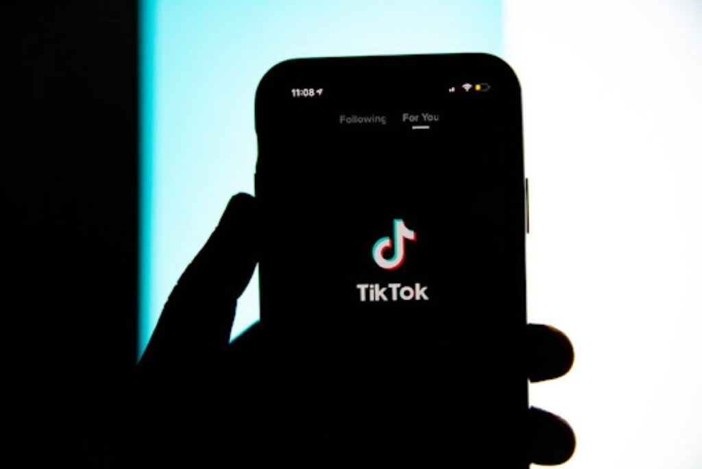 Silhouette of a hand holding a smartphone with a TikTok logo